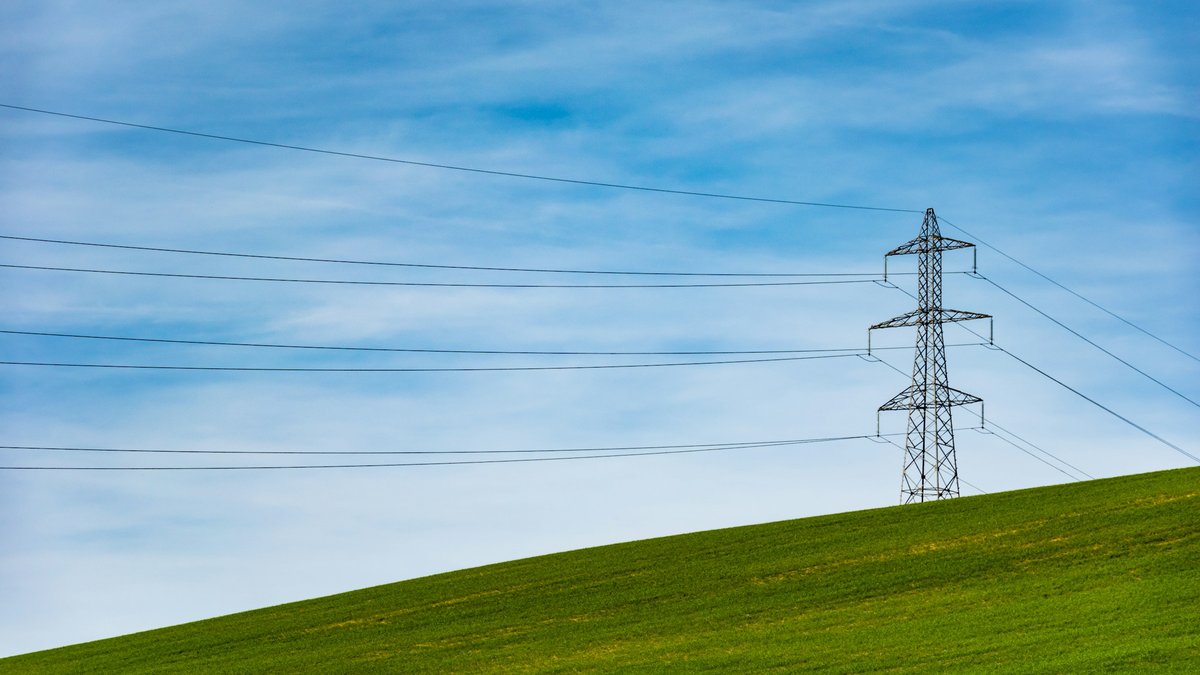 Hoogspanningsmast met transportkabels boven een groen weiland