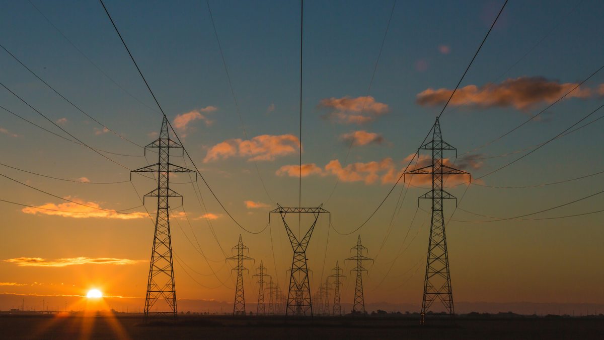 Hoogspanningsmasten tegen een oranje avondlucht bij zonsondergang